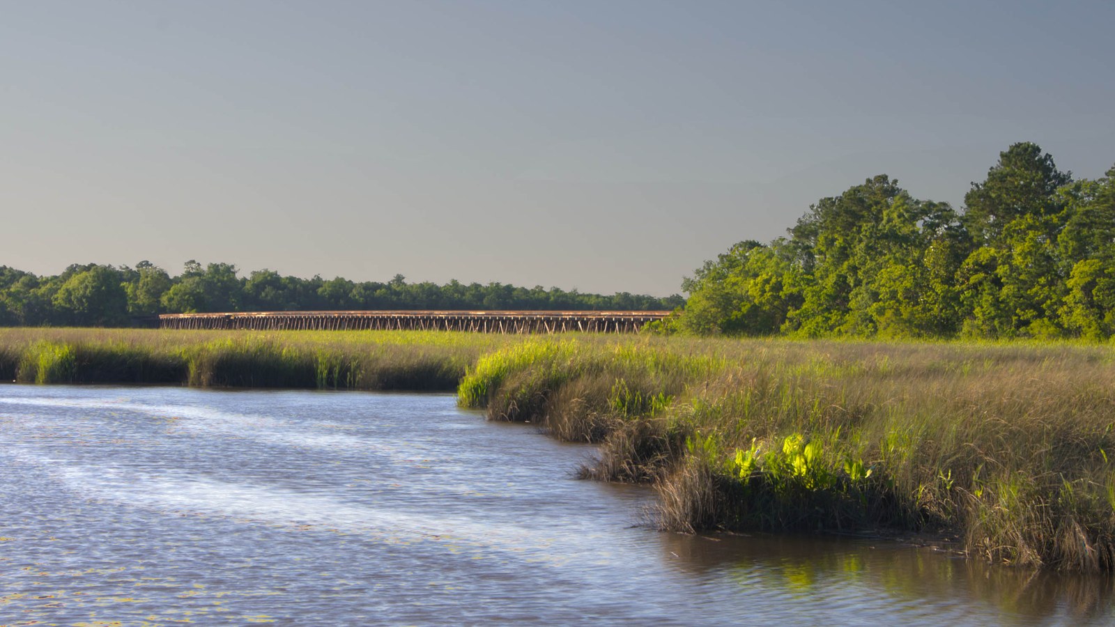 A wooden railroad trestle bridge crossing marshland near Hanahan at golden hour