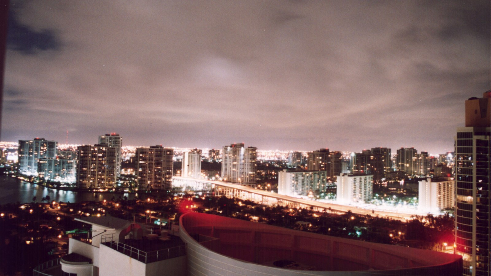 Aventura's cluster of high-rise waterfront condo towers lit up at night, seen across the water