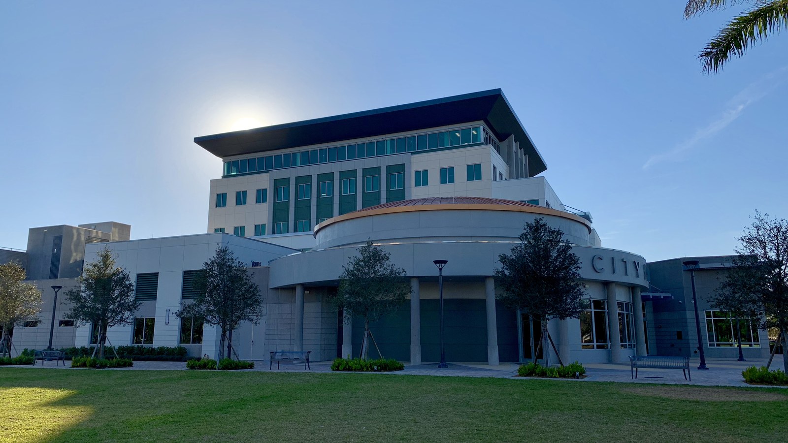 Coral Springs City Hall, a modern curved building fronted by palm trees under a partly cloudy sky