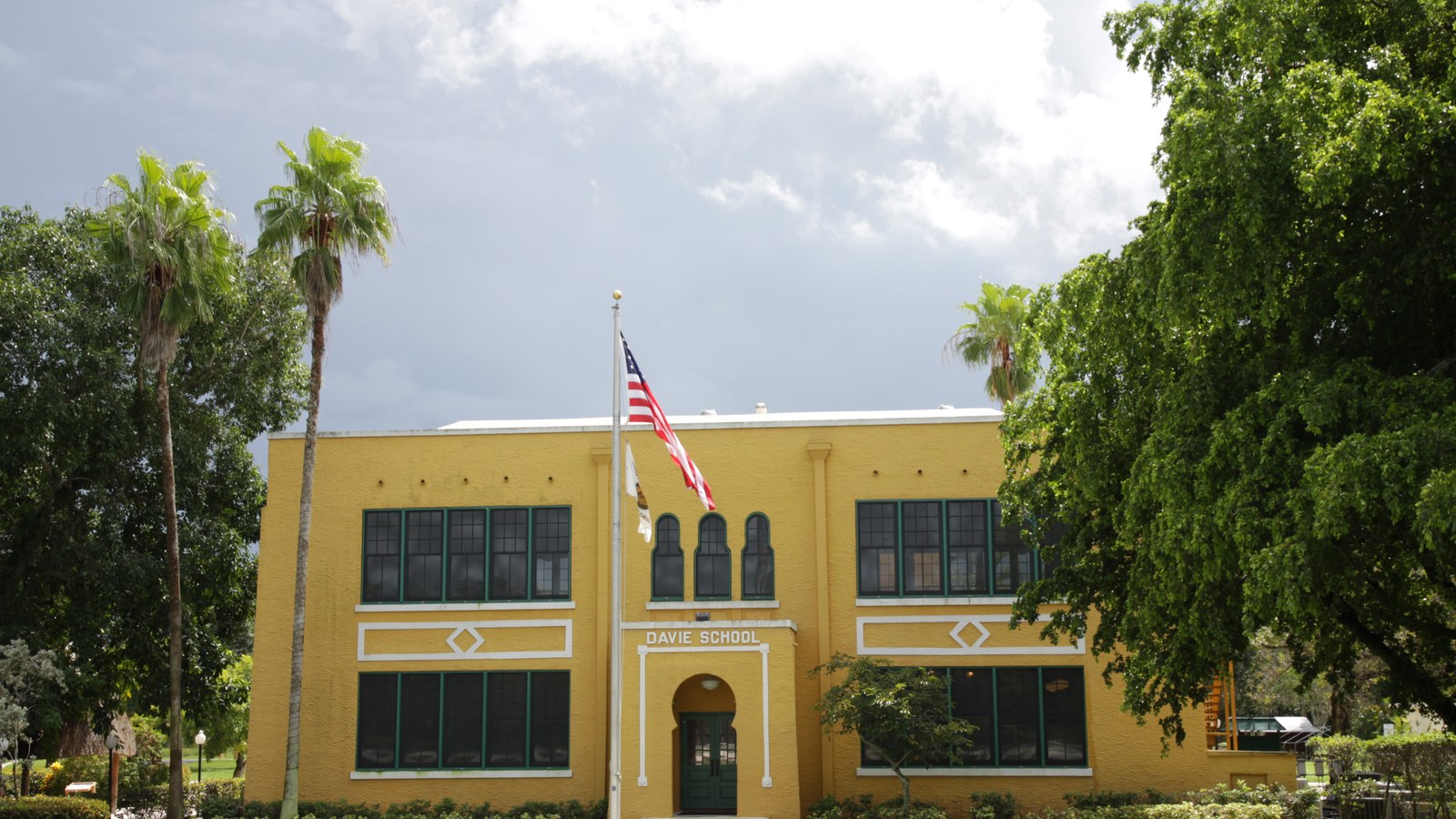 The historic Old Davie School, a yellow 1917 schoolhouse with green shutters, palm trees, and an American flag out front