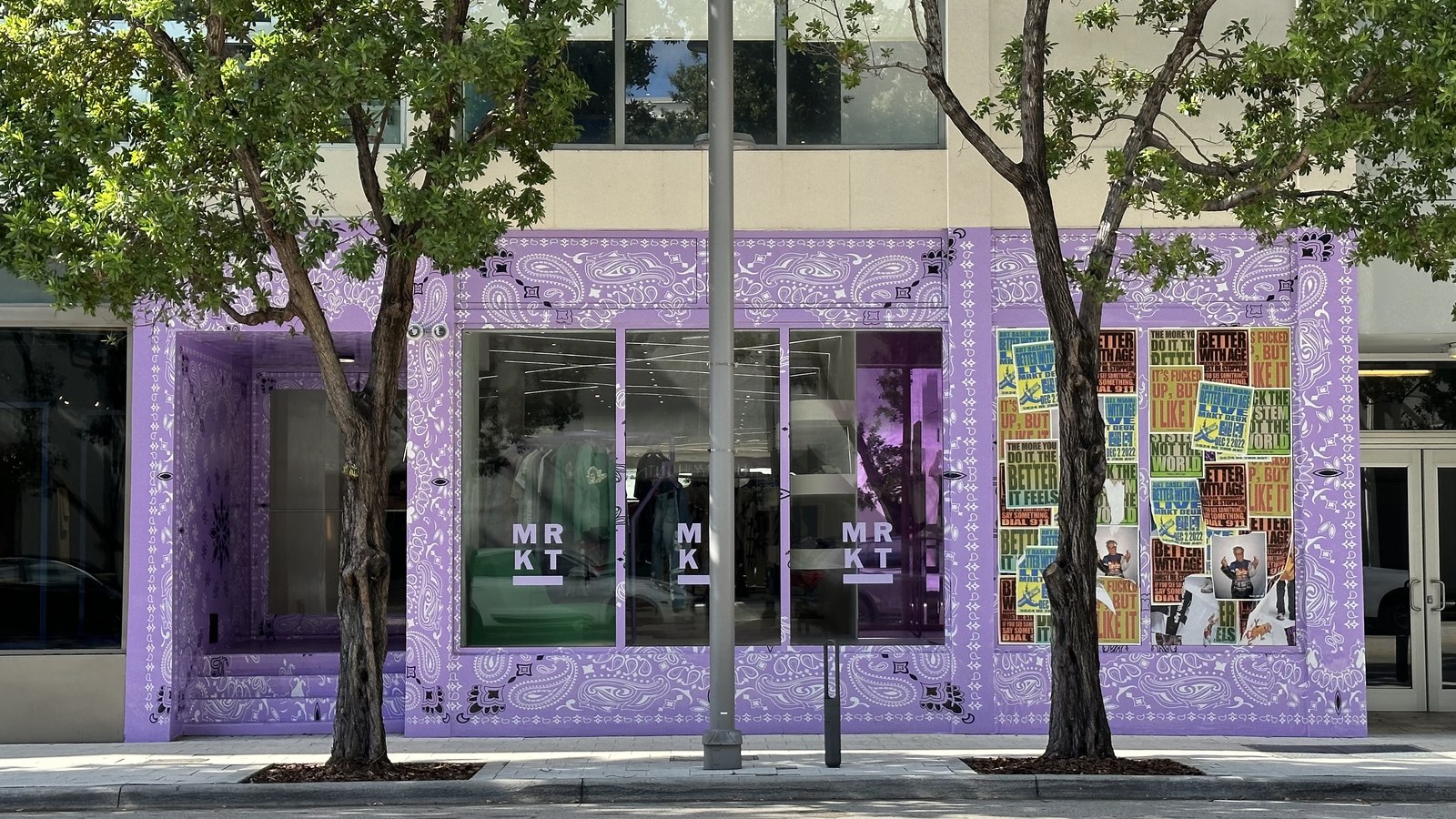 A boutique storefront with a paisley-patterned purple facade along a tree-lined sidewalk in the Miami Design District