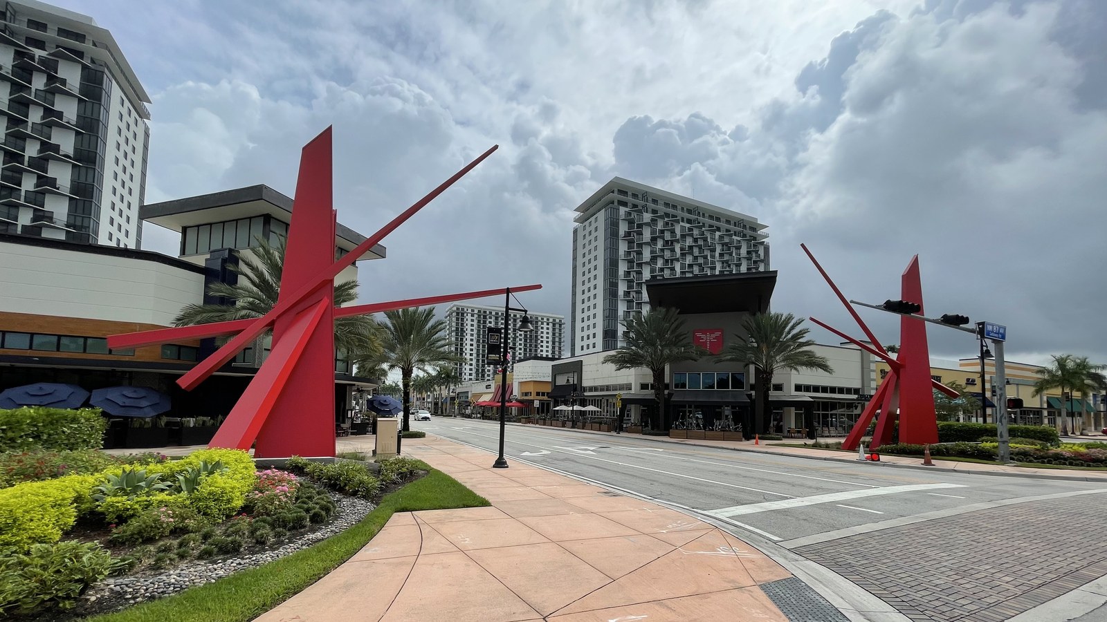 Downtown Doral's pedestrian plaza lined with shops and red sculptural art pieces, with mid-rise buildings behind