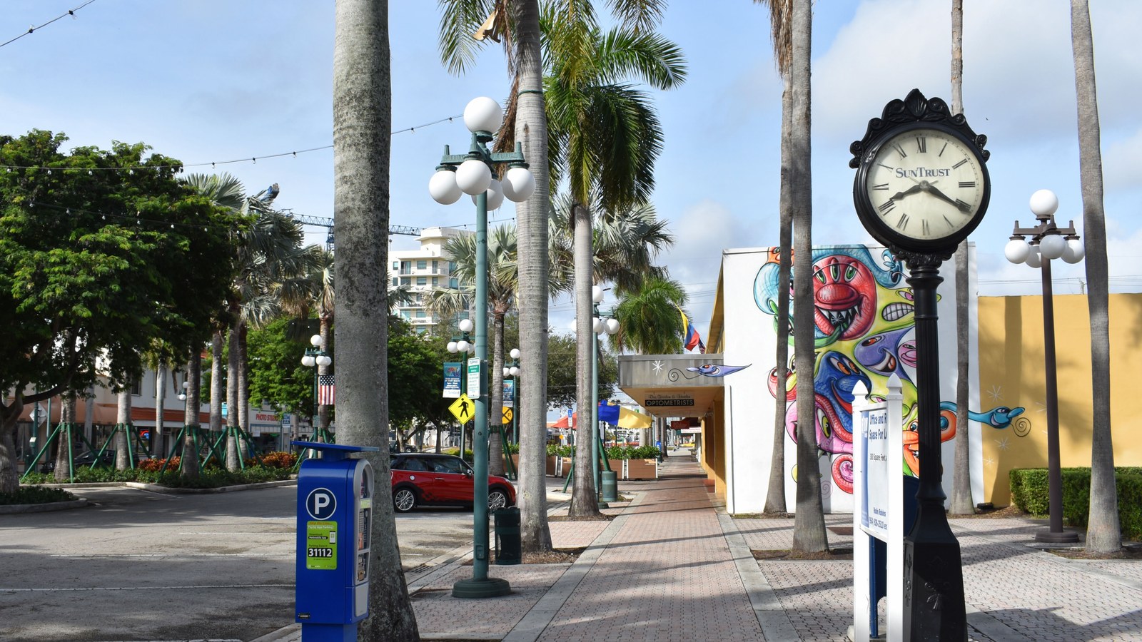 A palm-lined stretch of Hollywood Boulevard in downtown Hollywood, with a street clock, cafes, and a colorful mural