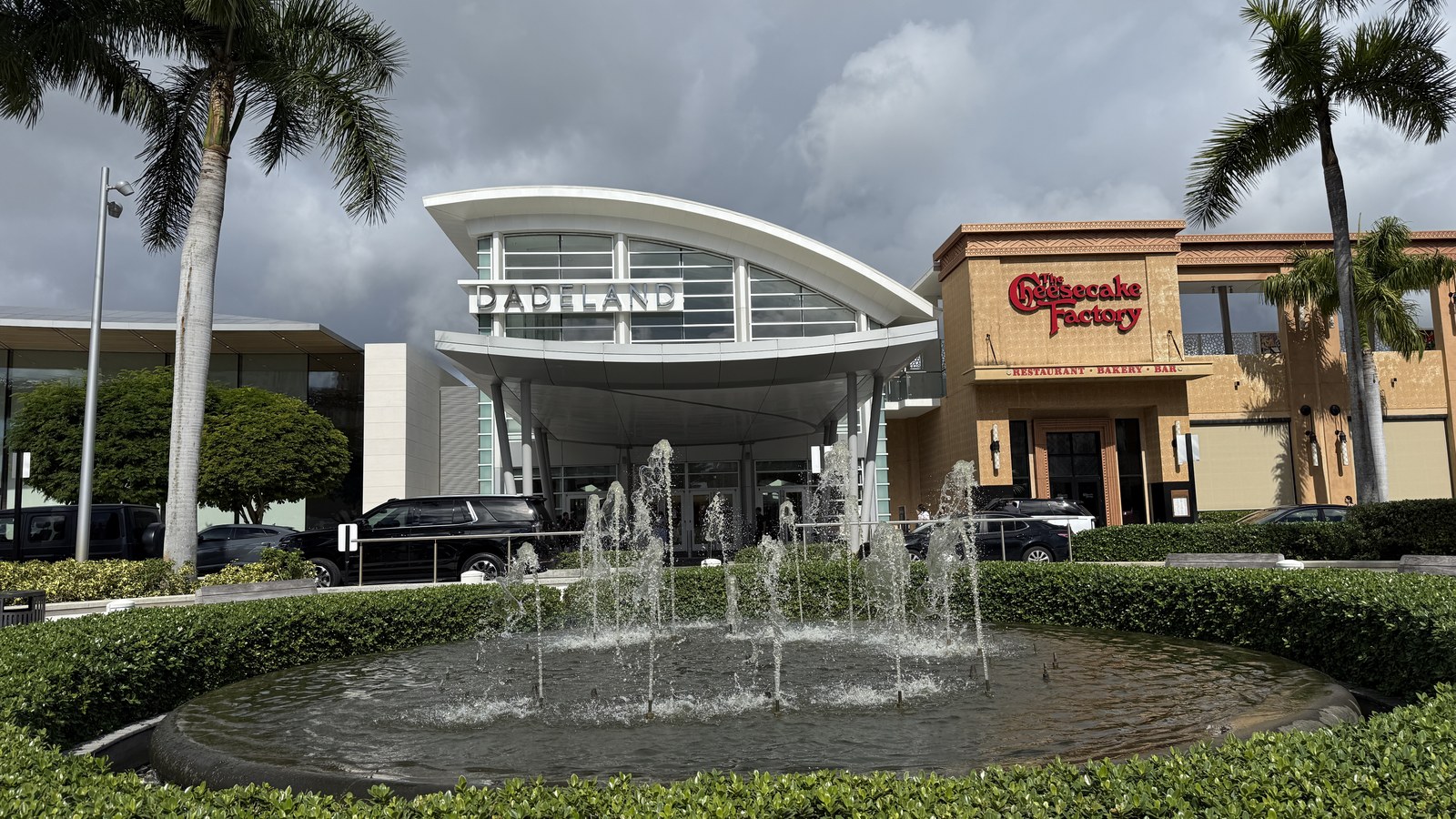 The curved white entrance canopy and fountain at Dadeland Mall's south entrance in Kendall, with the Cheesecake Factory alongside