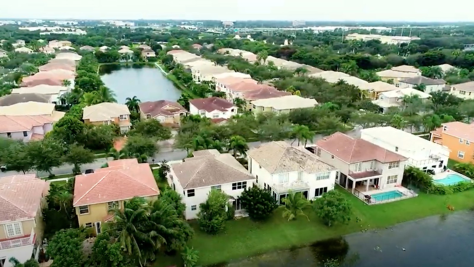 An aerial view of a Miramar residential neighborhood, with red-tile-roofed homes, pools, and a canal among the palm trees