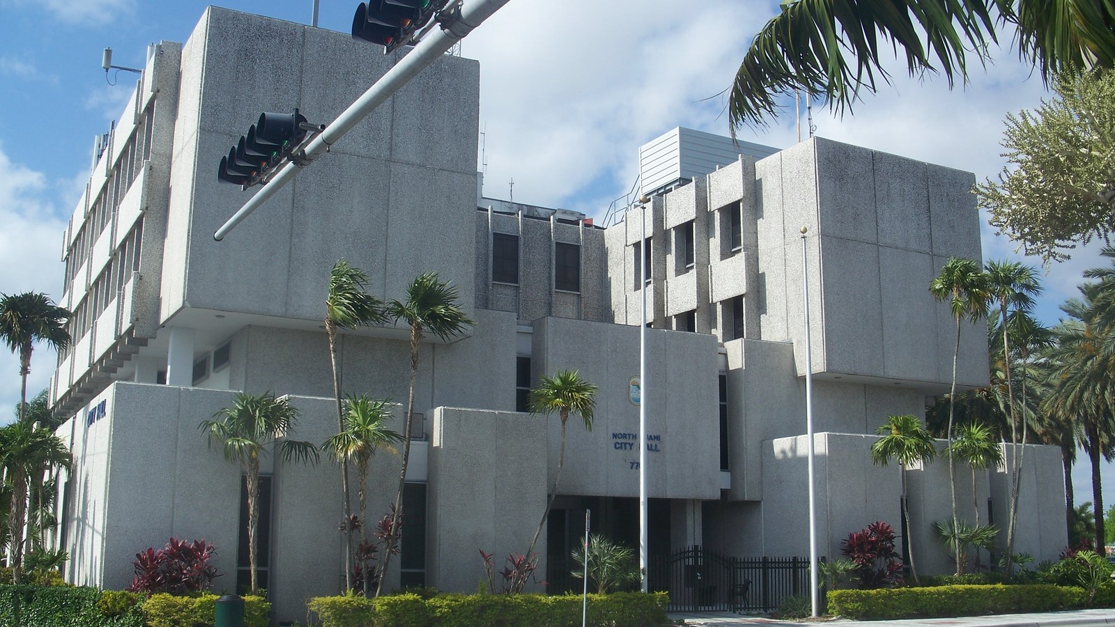North Miami's brutalist-style City Hall building, framed by palm trees under a blue sky