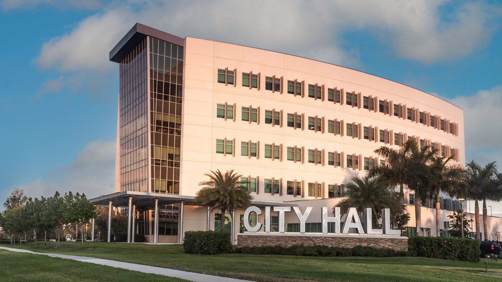 The City of Sunrise's City Hall building, a curved glass-and-stone office tower fronted by palm trees