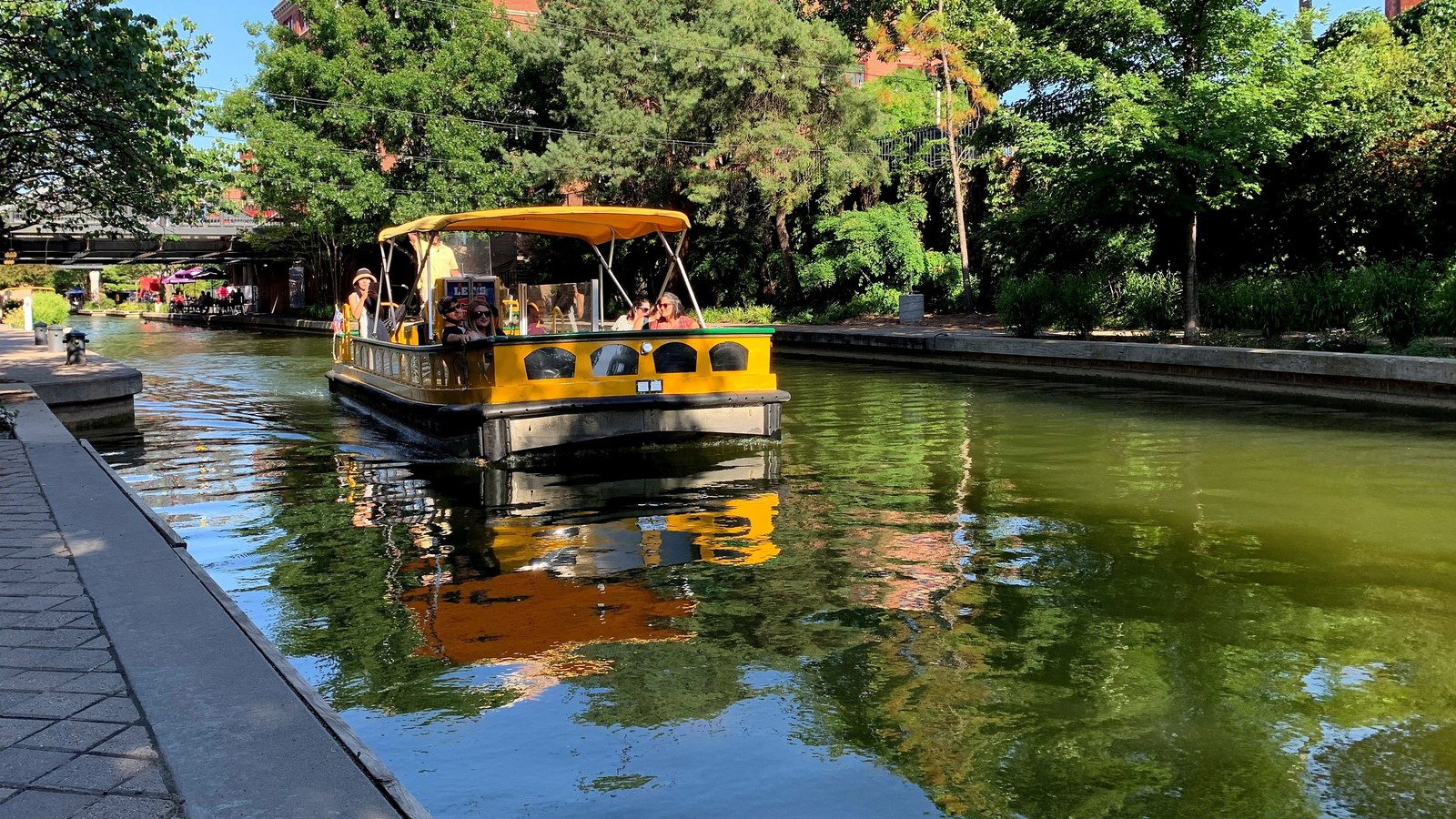 Bricktown Canal in downtown Oklahoma City, with a water taxi passing beneath the district's tree-lined banks