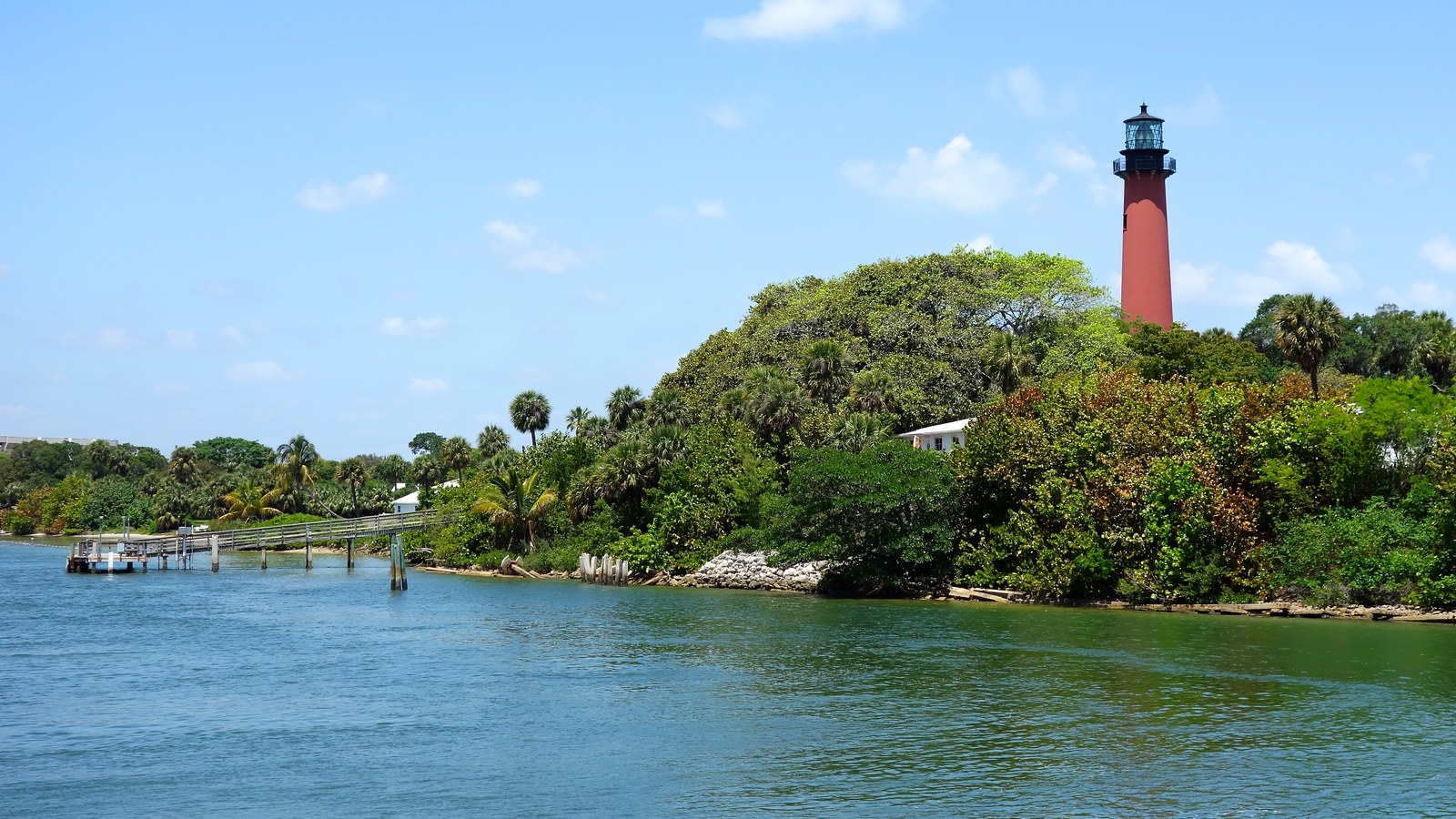 The red brick Jupiter Inlet Lighthouse rising above the trees on the Loxahatchee River, seen from across the water