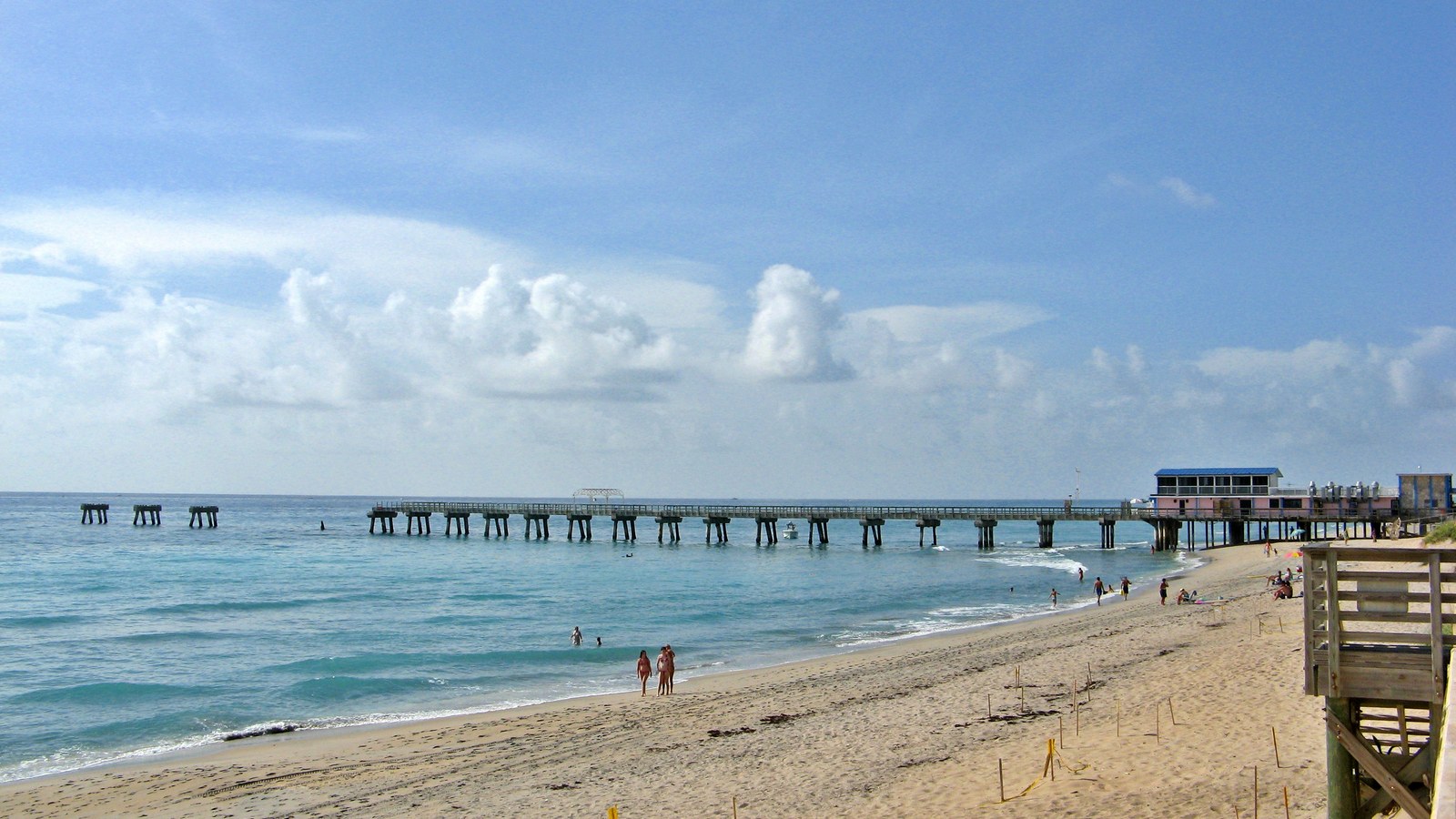 The Lake Worth Beach municipal pier extending into the Atlantic Ocean, with swimmers and sunbathers on the beach