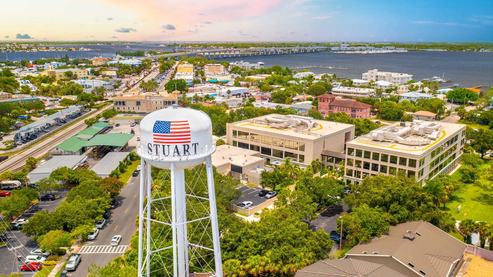 An aerial view of downtown Stuart at sunset, with the STUART water tower in the foreground and the St. Lucie River and Roosevelt Bridge behind it