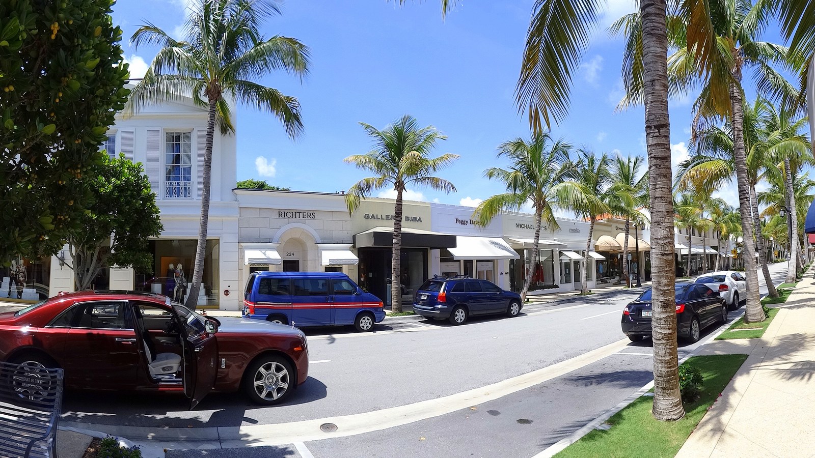 Worth Avenue in the Town of Palm Beach, lined with palm trees, luxury storefronts, and parked cars