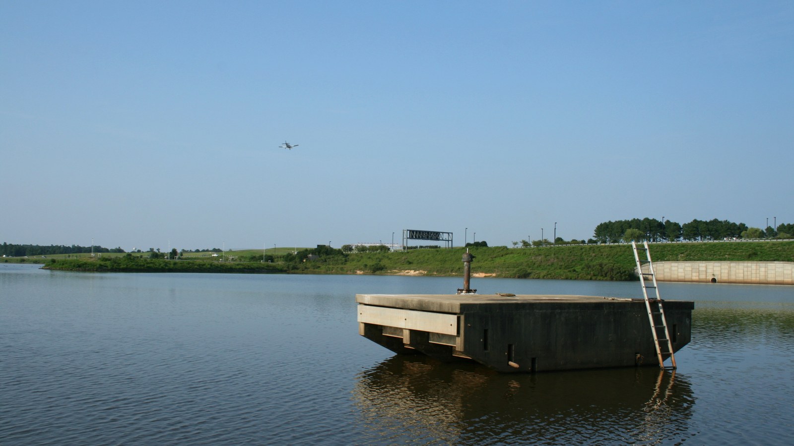 The spillway at Brier Creek Reservoir in northwest Raleigh, with a small aircraft on approach to RDU visible in the distance