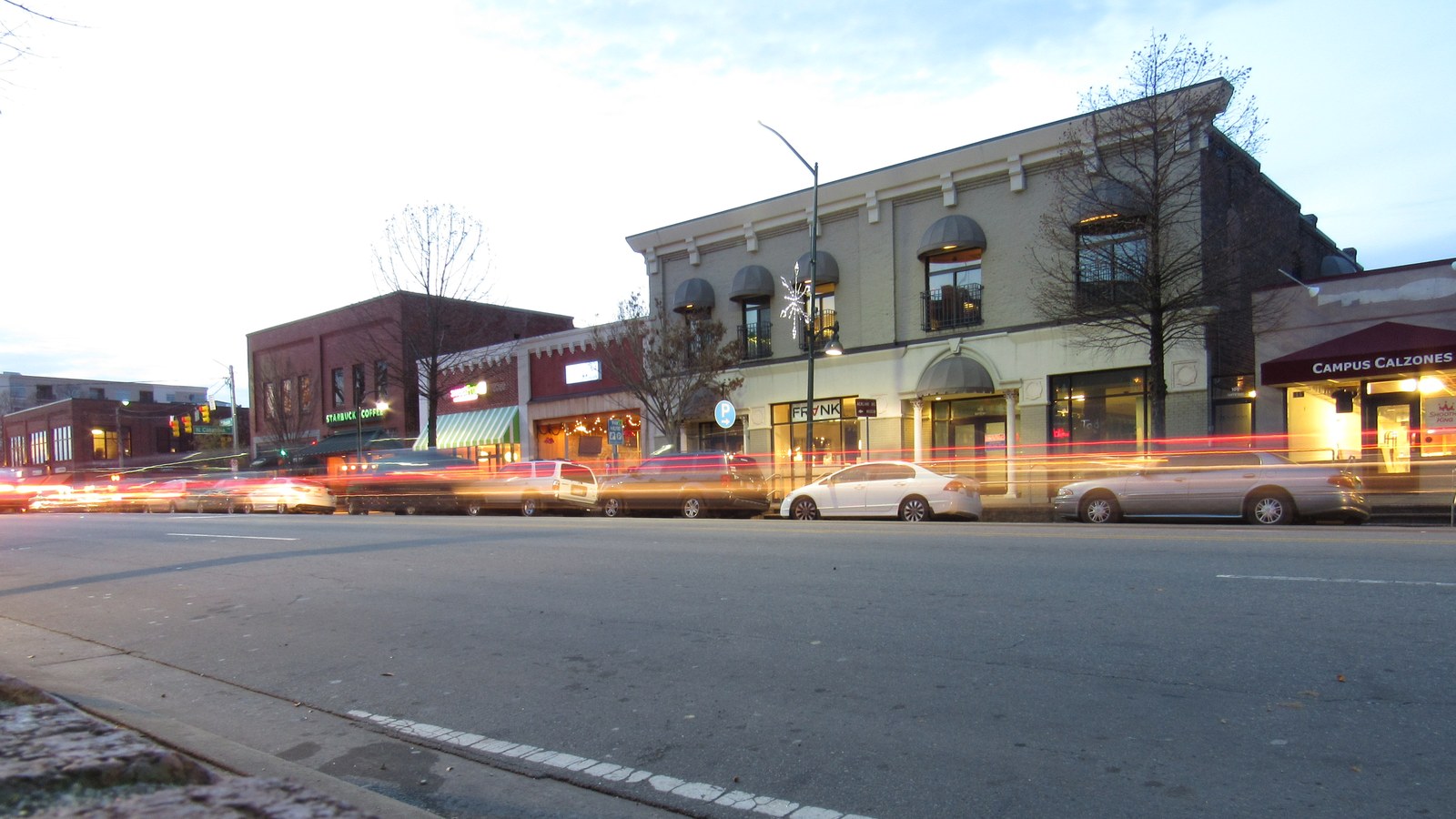 Storefronts along Franklin Street in Chapel Hill at dusk, with light trails from passing traffic