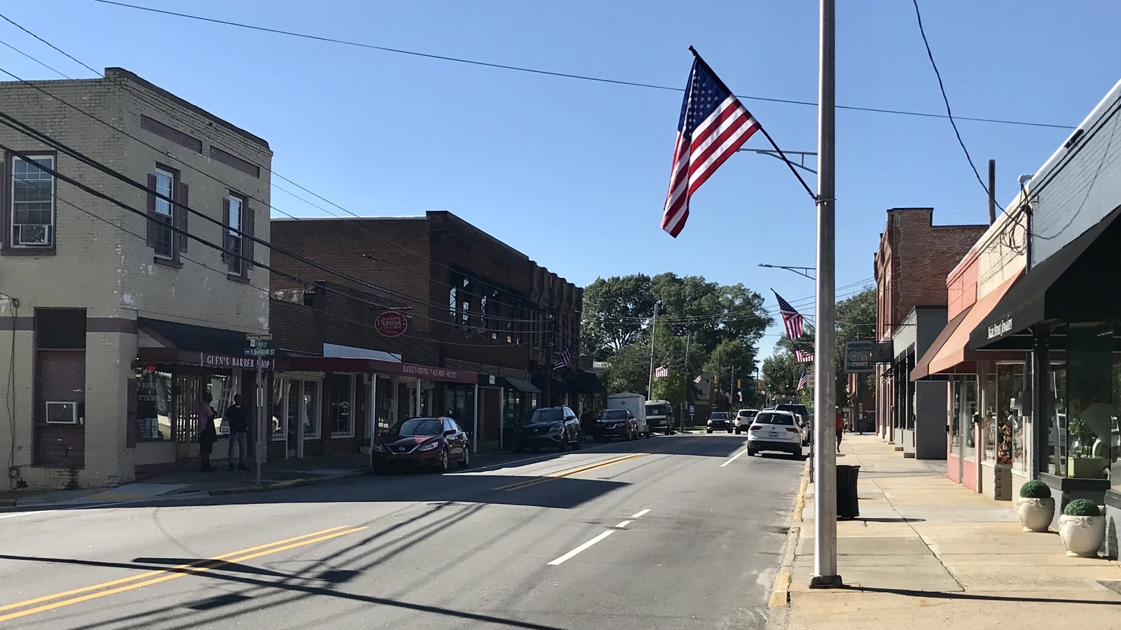 East Main Street in downtown Clayton with brick storefronts and an American flag flying over the sidewalk