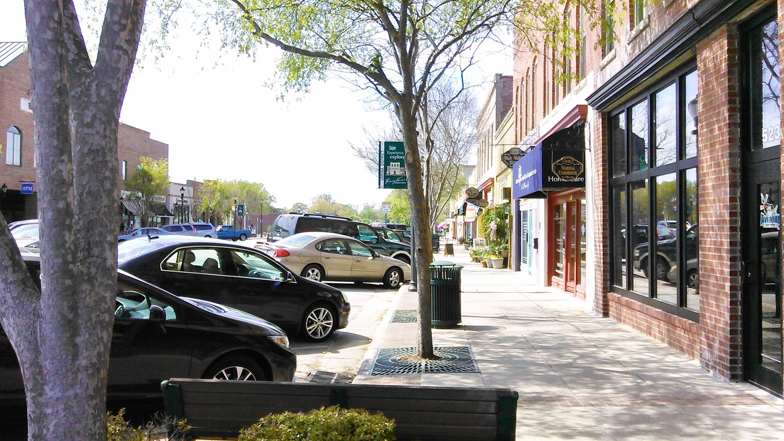 Historic Downtown Fuquay-Varina street scene with brick storefronts, a leafy sidewalk, and parked cars