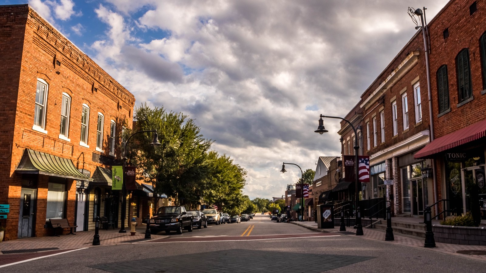 Row of brick buildings along White Street in downtown Wake Forest under a dramatic sky