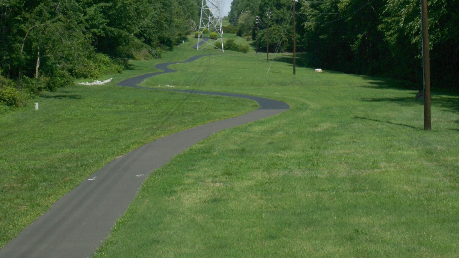 A paved greenway jogging trail winding through a grassy corridor under power lines in the Woodcroft neighborhood of South Durham