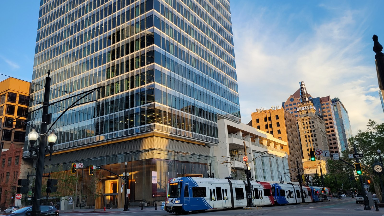 A TRAX light-rail train on Main Street in downtown Salt Lake City at golden hour, with the 111 Main tower and the historic Walker Center building behind it
