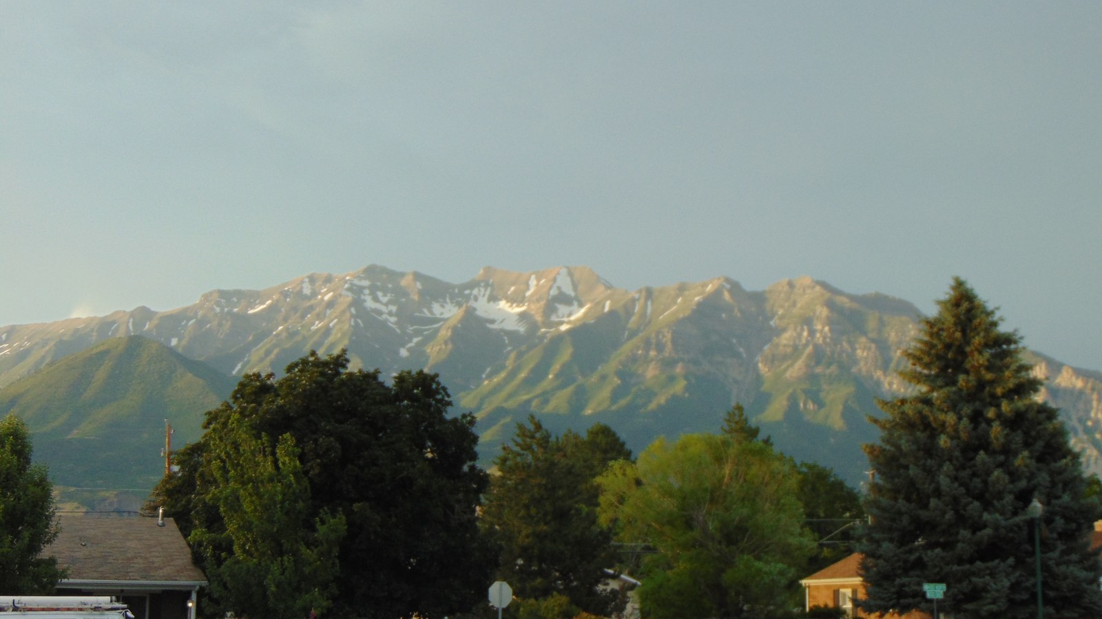 Mount Timpanogos rising behind a tree-lined residential street in Orem, Utah, its upper slopes lit gold at sunset