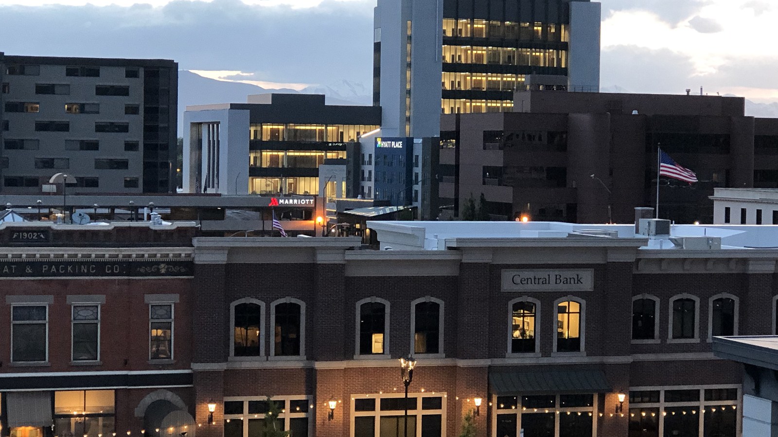 Downtown Provo, Utah at dusk, with the lit Marriott and Hyatt Place towers behind the brick storefronts of Center Street's Central Bank building