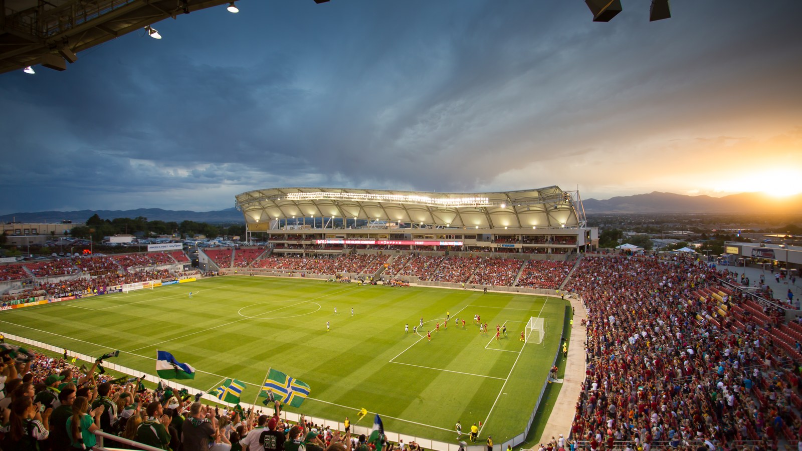 A packed America First Field at sunset during a Real Salt Lake match in Sandy, Utah, with the stadium's canopy roof silhouetted against storm clouds