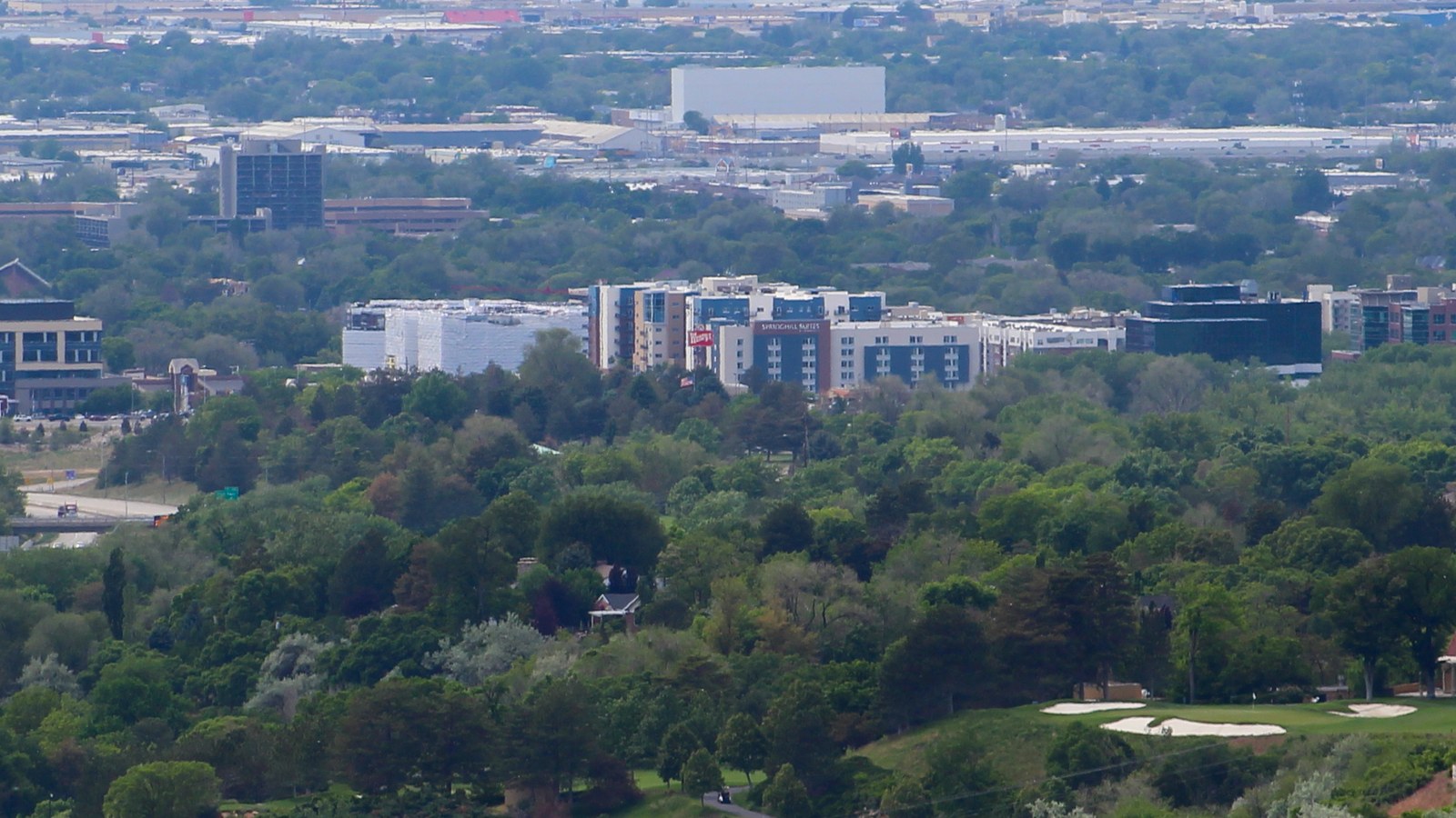 Aerial view of Sugar House's commercial core in Salt Lake City, with mid-rise mixed-use buildings surrounded by tree canopy, seen from Grandeur Peak