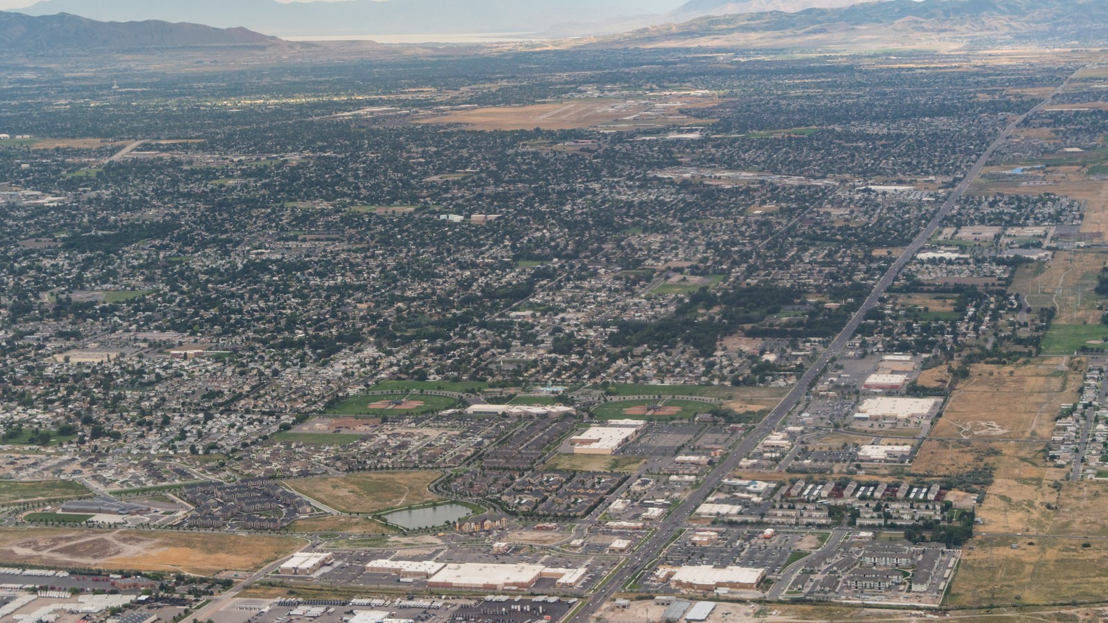 Aerial view of West Valley City, Utah, showing dense residential subdivisions, a shopping center, and the Salt Lake Valley floor toward the Great Salt Lake and mountains