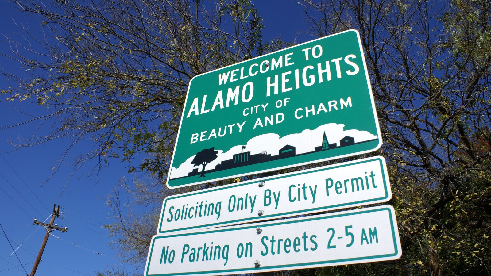 A "Welcome to Alamo Heights, City of Beauty and Charm" sign at the city's edge